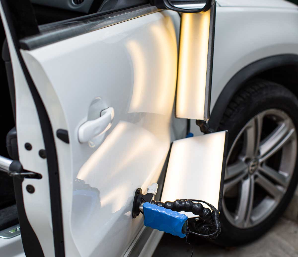 Paintless dent repair tools working a vehicle panel